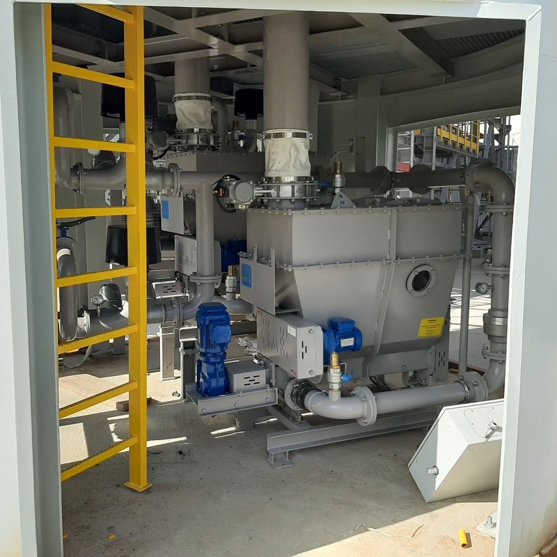 Two dosing devices arranged in a redundant system are located beneath the lime silo. The devices are grey in color, with visible blue electric drives. Additionally, grey pipelines can be seen, as well as a ladder inside the dosing silo. The lime is discharged into the dosing units via a flexible sleeve equipped with electric dampers.